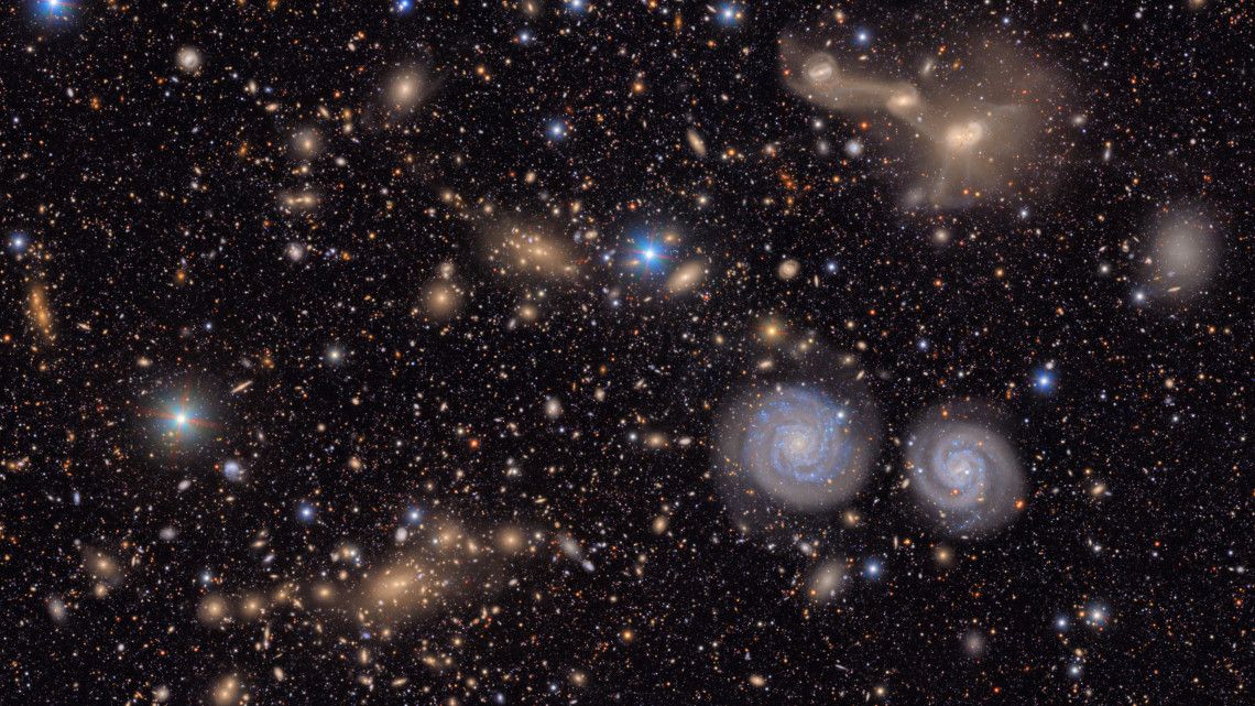 the cosmos showcasing many stars and two different spiral-shaped galaxies.
