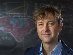 Jonathan Mattingly smiles at the camera in front of a blackboard with a map of the USA drawn on it.  